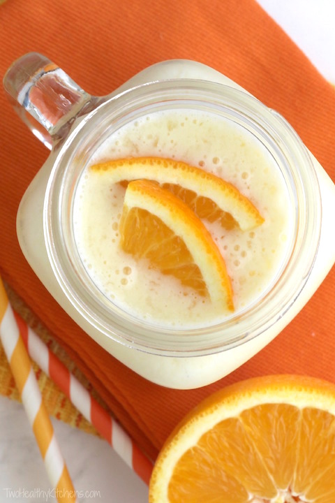 Top-down view of a smoothie in a glass mug with orange slices on top and nearby.