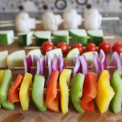 Several skewers, each threaded with a different kind of vegetable, lined up on cutting board.