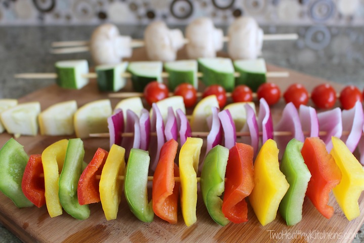 Several skewers, each threaded with a different kind of vegetable, lined up on cutting board.