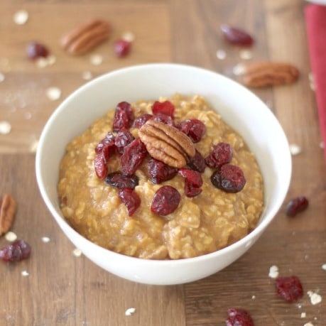 Photo os a white bowl of Pumpkin Oatmeal, garnished with dried cranberries and a pecan half.