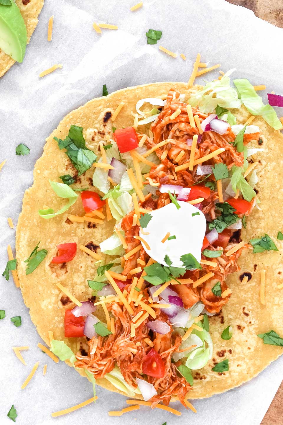Overhead photo of one crock pot chicken taco, laying open to show the chicken topped with a variety of Mexican toppings.