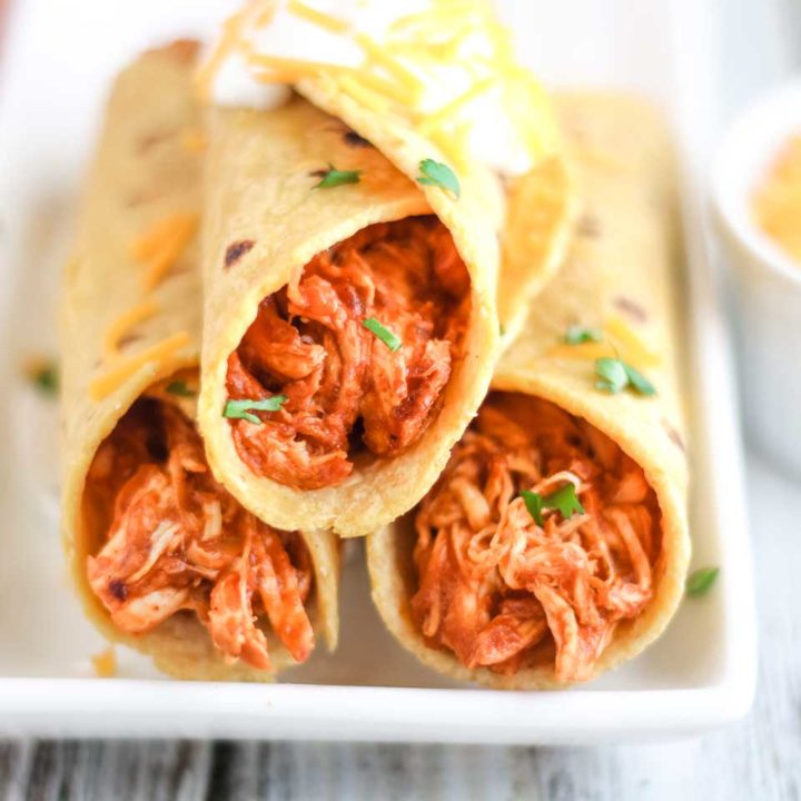 A stack of 3 crock pot chicken tacos on a long white serving plate, made very simply with just the slow cooker chicken taco meat wrapped in corn tortillas.