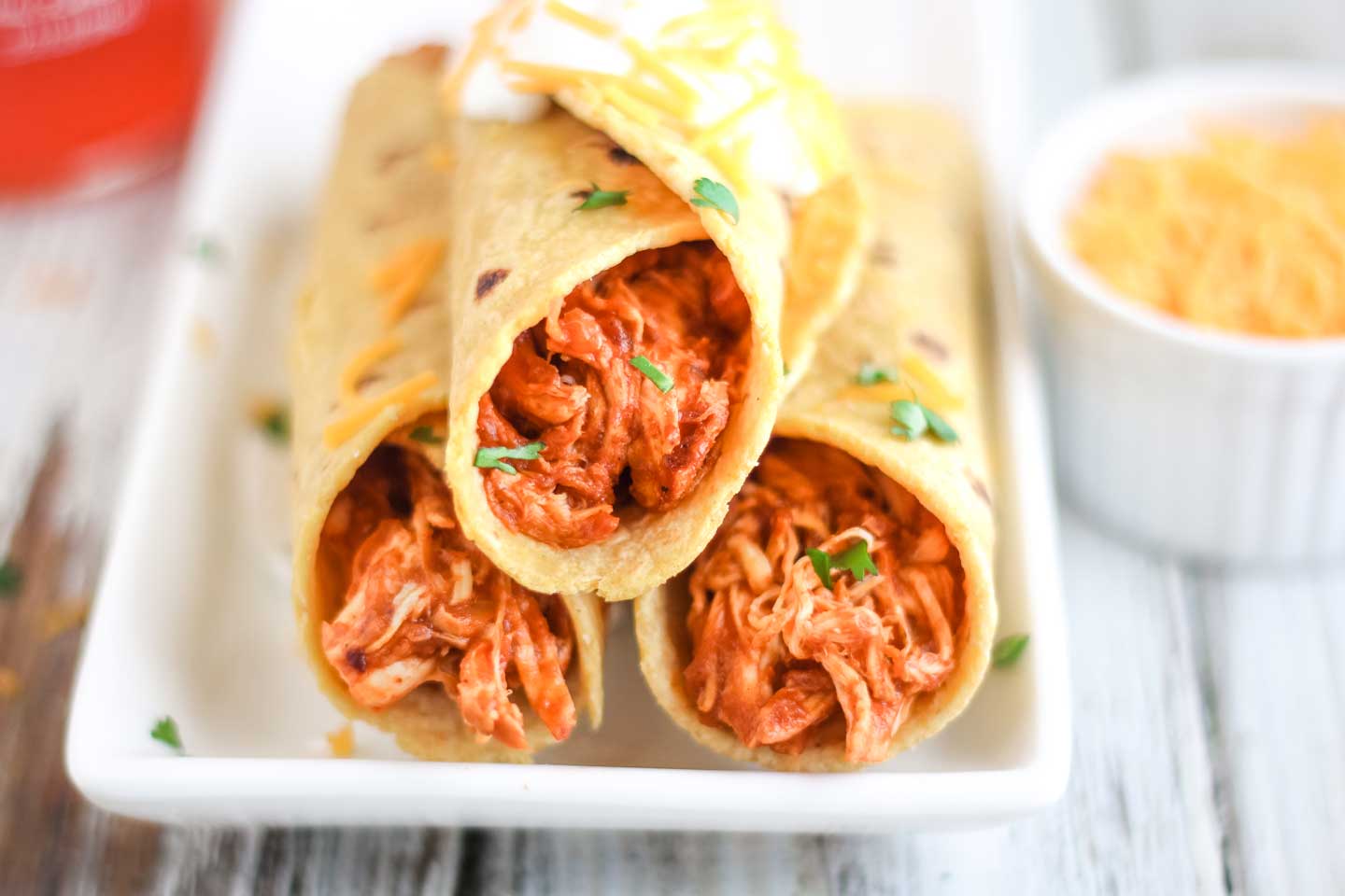 A stack of 3 crock pot chicken tacos on a long white serving plate, made very simply with just the slow cooker chicken taco meat wrapped in corn tortillas.