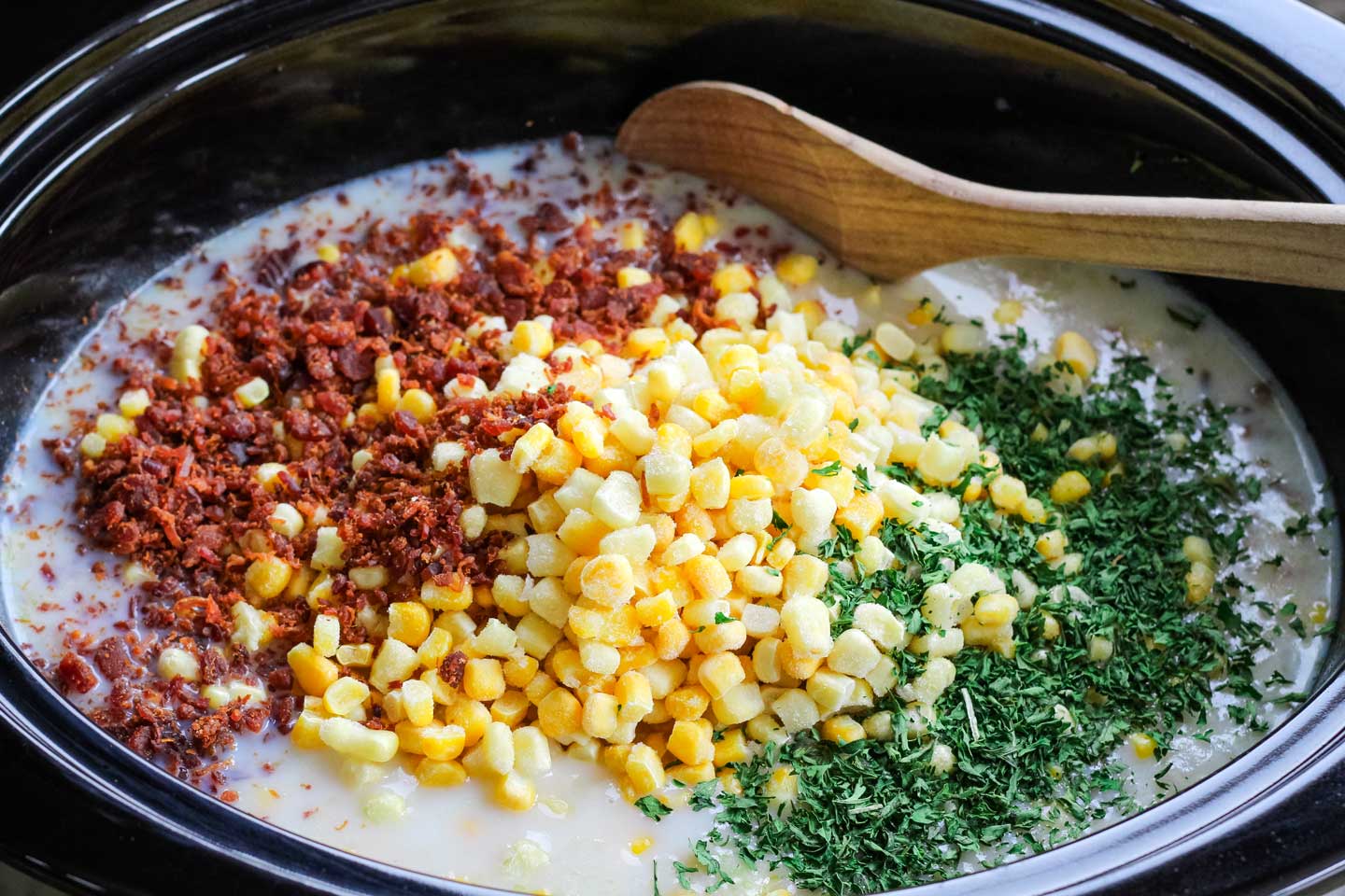 overhead of the next step, with dried parsley and bacon crumbles added to the slow cooker on top of the frozen corn