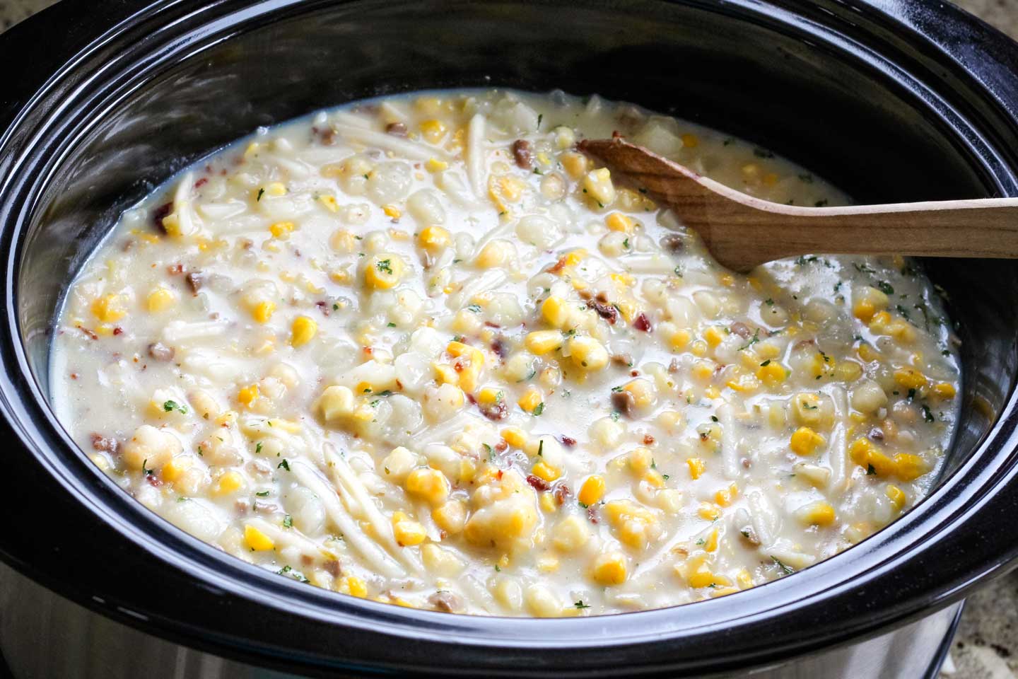 overhead of the finished Chicken Corn Chowder recipe, still in the crock pot, with a wooden spoon stirring