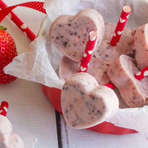 Pinnable image of the Greek Yogurt Bites shaped like hearts with heart-printed straws for sticks, piled in a low red bowl.