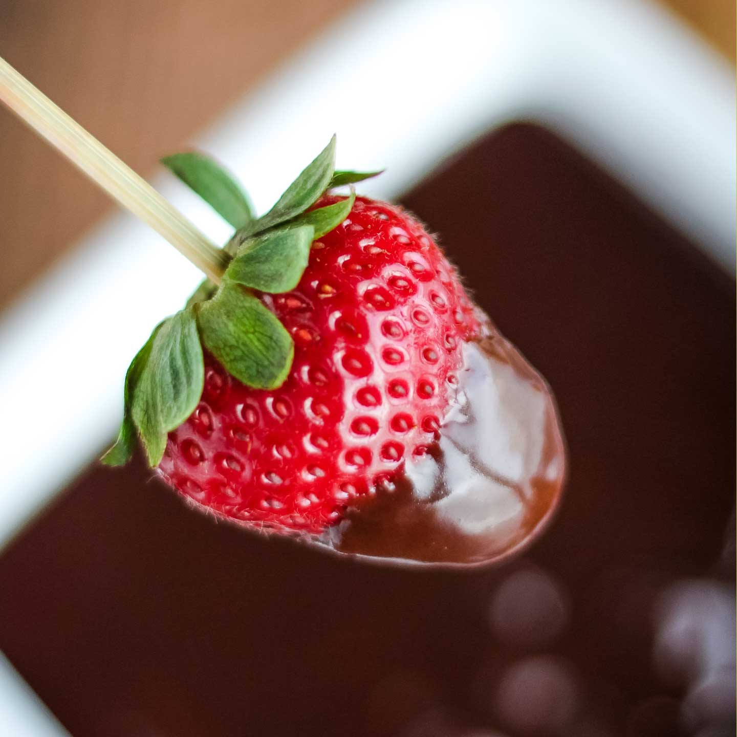 closeup of fresh strawberry on a skewer, that's been partially dipped into the Chocolate Dip bowl below
