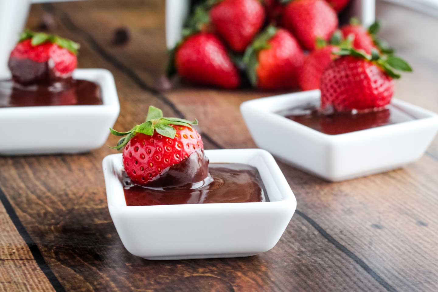 three little white, square bowls of Chocolate Dip, with one strawberry sitting in each
