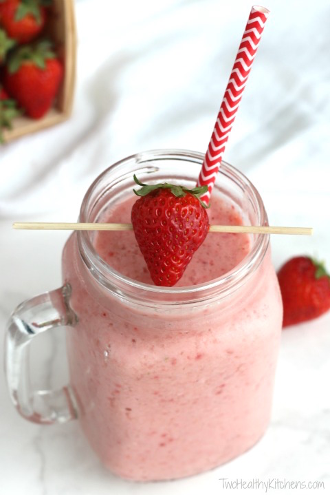 smoothie in clear glass mug with a decorative paper straw and a garnish of a skewered strawberry