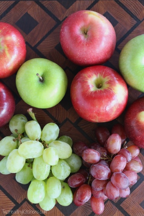 Overhead of several apples (red and green) plus a sprigs of red and green grapes on a patterned wood cutting board.