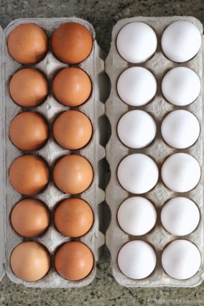 Overhead of two dozen eggs in cartons, side-by-side - one brown eggs and one white eggs.