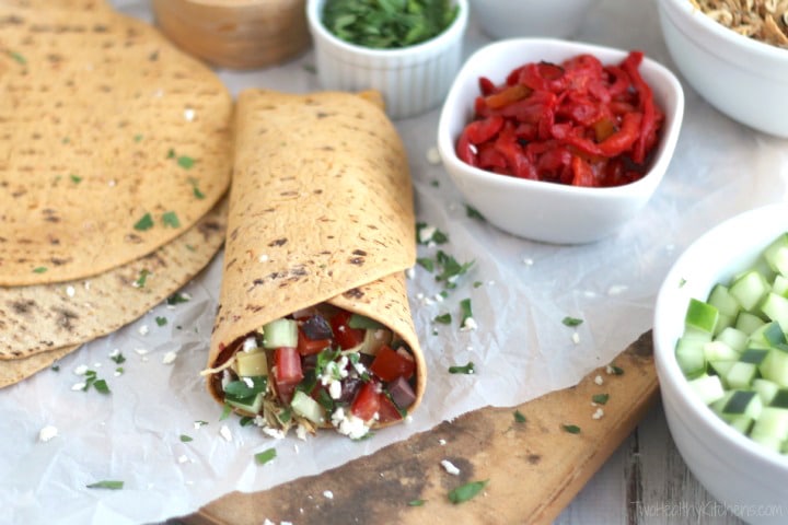 One large, rolled-up taco on white paper with extra wraps and toppings nearby.