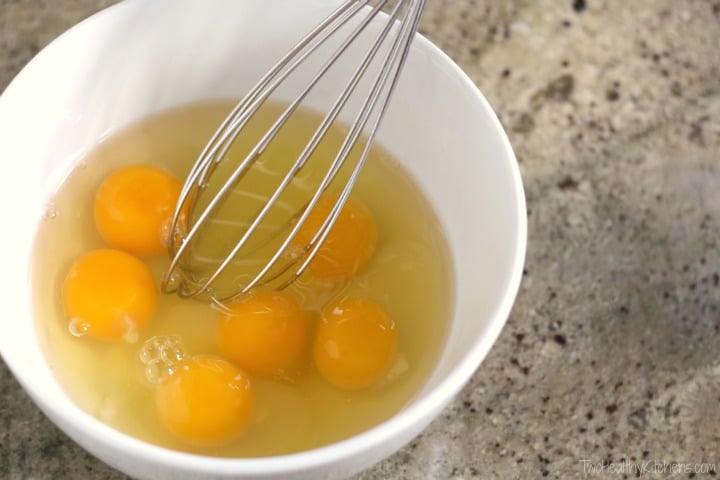 Whisk just beginning to stir 6 eggs in a white bowl.