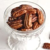 Glass parfait dish filled with candied pecans, with two extras lying next to it.