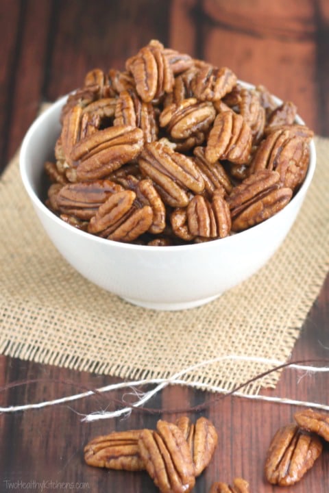 Candied pecans piled in white bowl on burlap with gift twine and extra nuts in foreground.