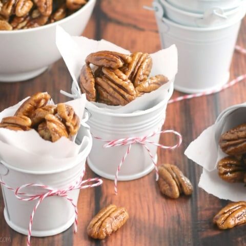 Finished nuts in decorative little white pails tied with Christmas twine, with bowl of more candied pecans and more pails in background.