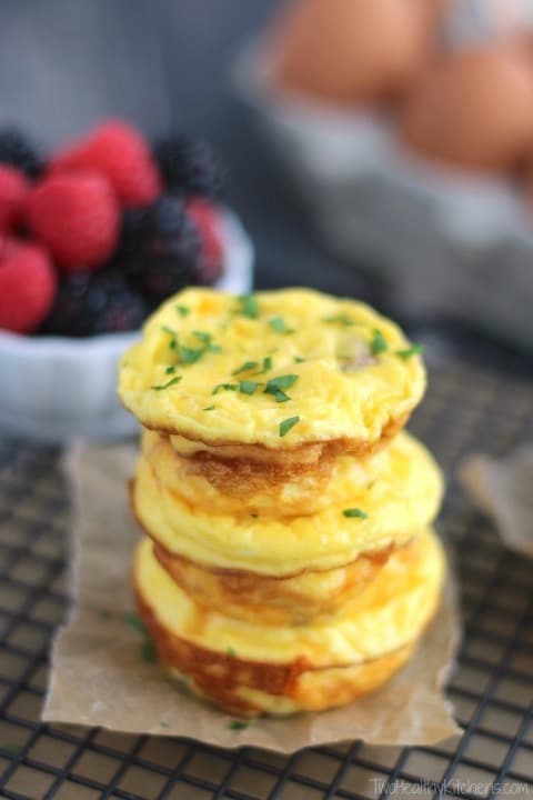 Stack of 3 egg muffins on square of brown parchment on cooling rack; bowl of berries and carton of brown eggs in behind.
