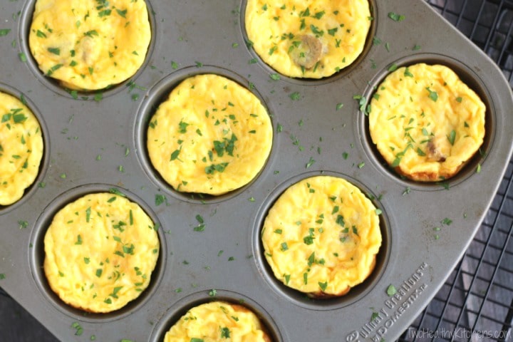 Overhead of muffin pan with baked egg cups sprinkled with chopped parsley, diagonally laid on cooling rack.