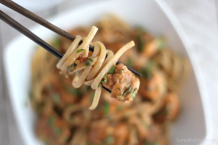 Closeup of chopsticks holding twirl of pasta with chunk of salmon, with bowlful fuzzy below.