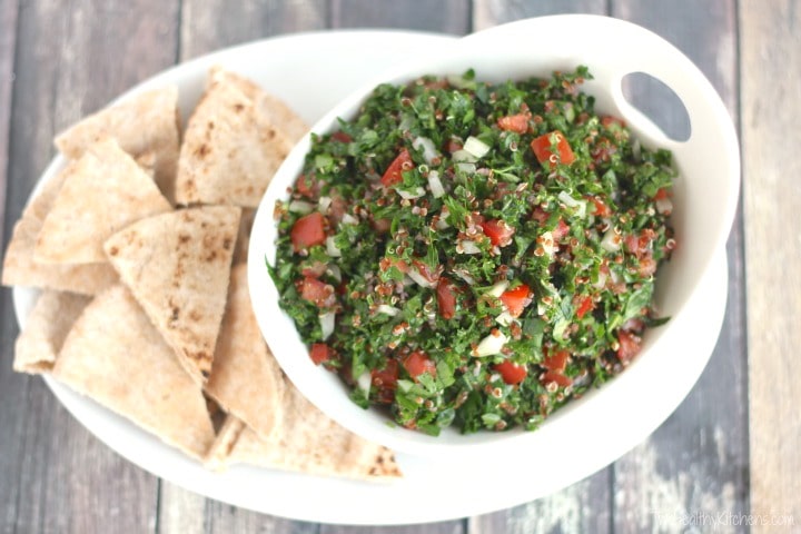 Curved serving bowl of quinoa tabouli on white platter surrounded by pita wedges.