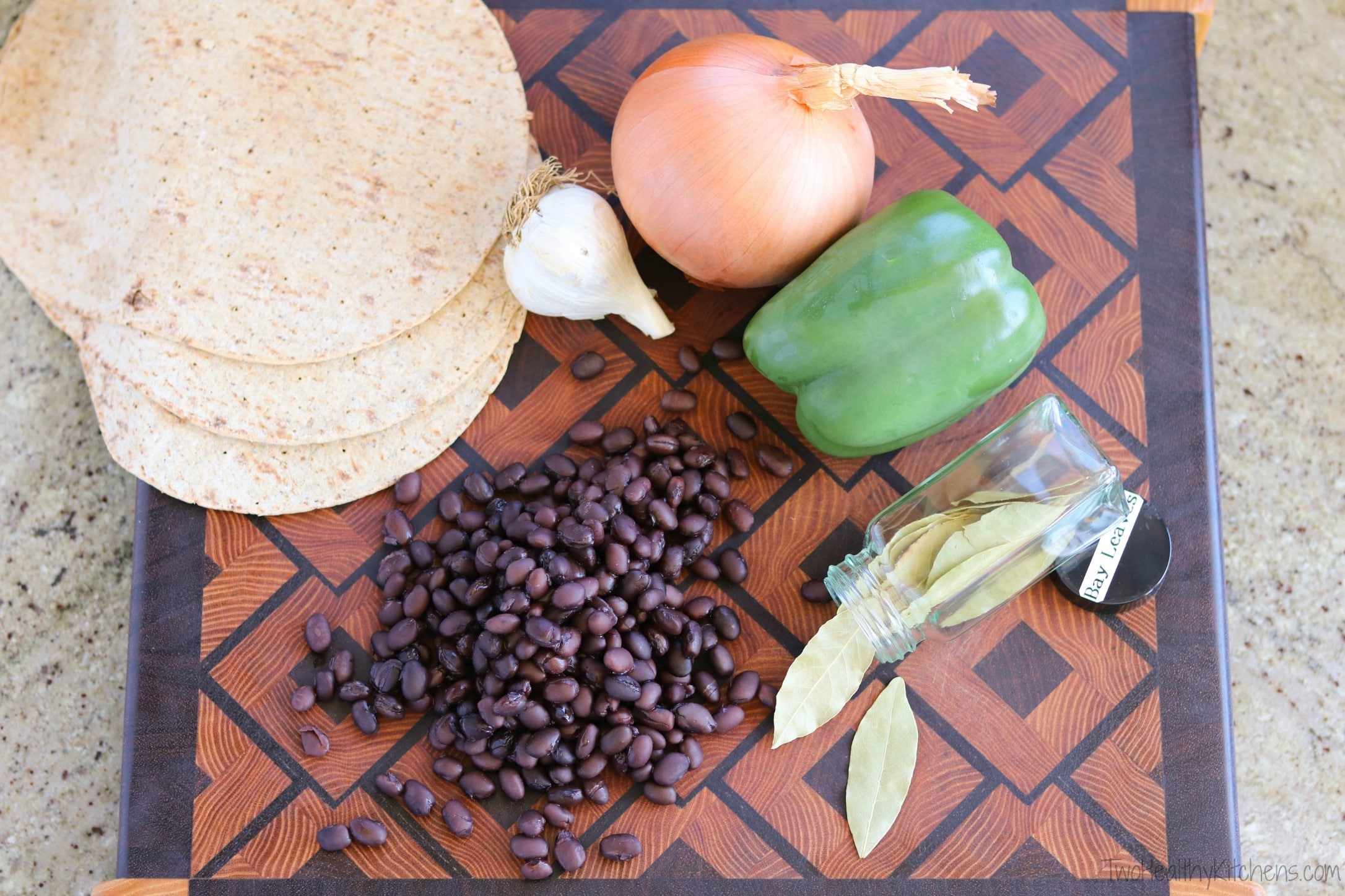 Ingredients on cutting board - black beans, vegetables, flatbreads and jar of bay leaves.