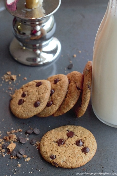 Several cookies propped against a glass jar of milk.