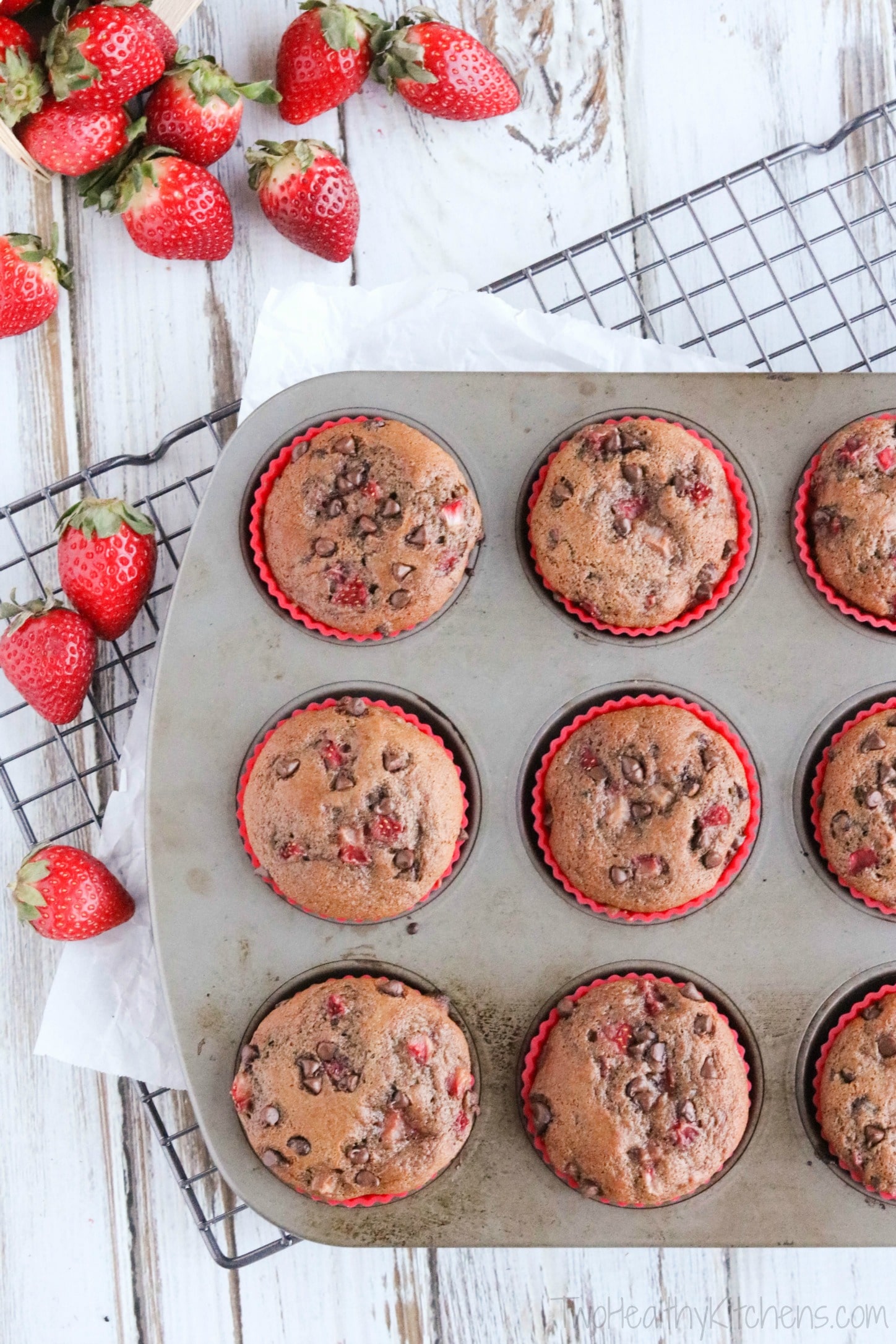 Overhead photo of muffins still in muffin pan on cooling rack with fresh strawberries decoratively nearby.