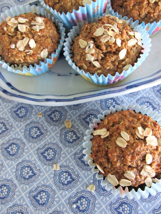 Several muffins on blue-rimmed plate with one out front on blue-patterned counter.