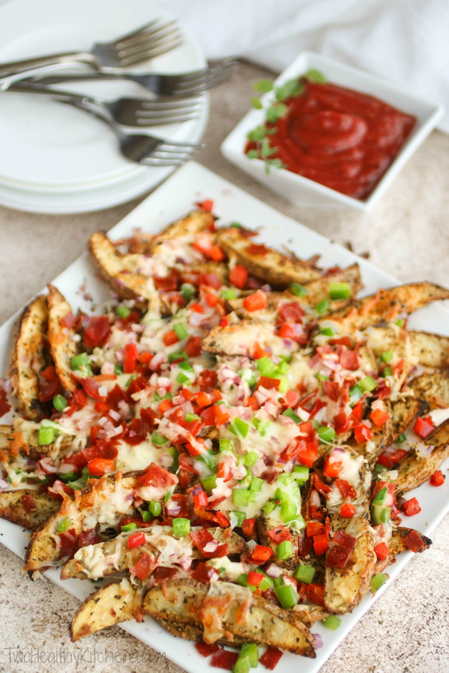 Pizza fries on square serving platter with dish of pizza sauce dip and appetizer plates in background.
