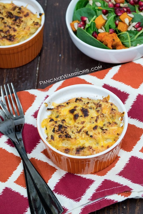 One orange ramekin of healthy mac and cheese on red and orange patterned napkin with forks, bowl of salad and second ramekin nearby.