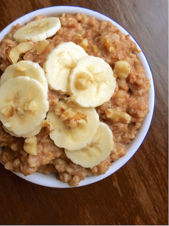 Overhead of oatmeal in white bowl, topped with sliced banana.