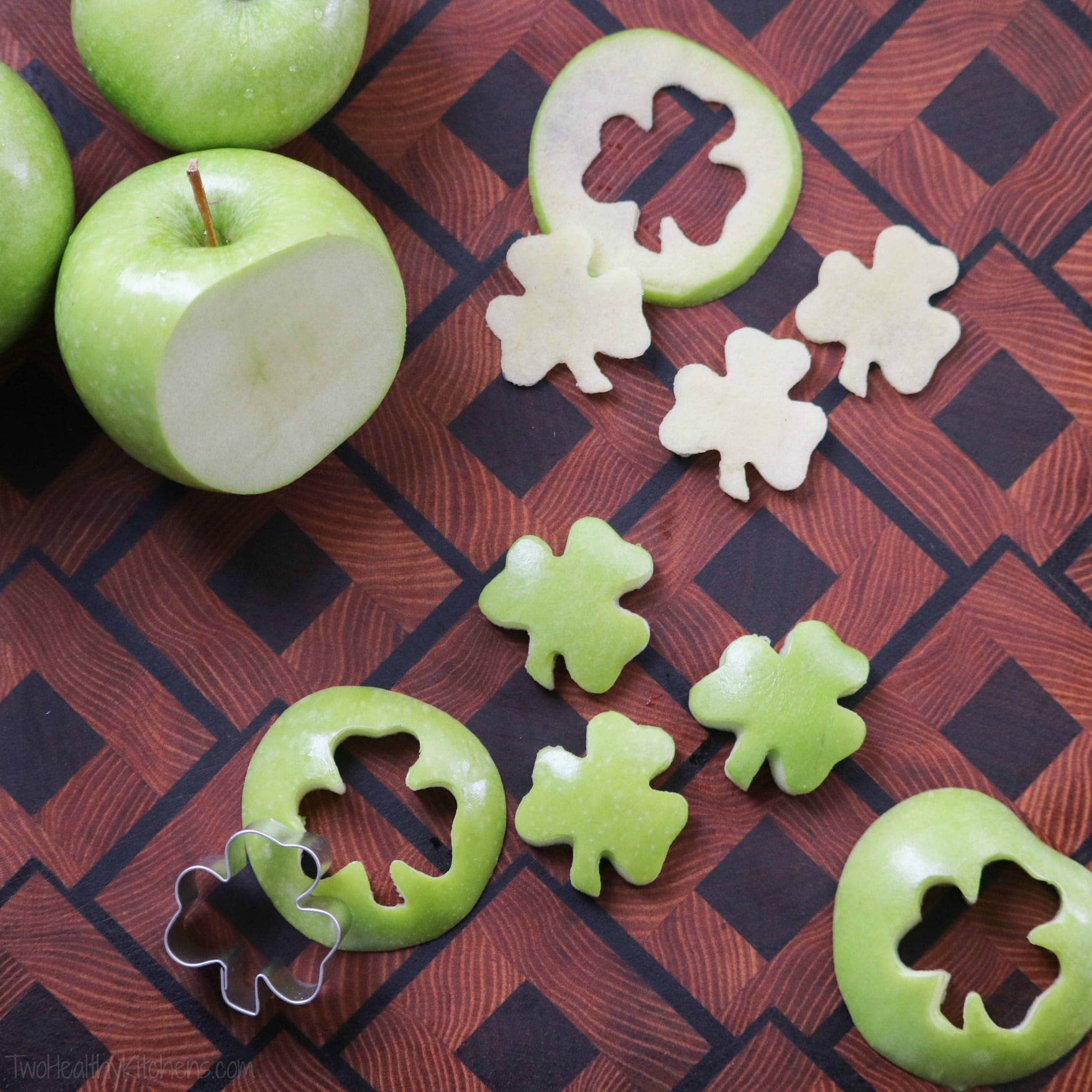 Green apples on patterned-wood cutting board, sliced and cut into shamrocks using cooking cutter.