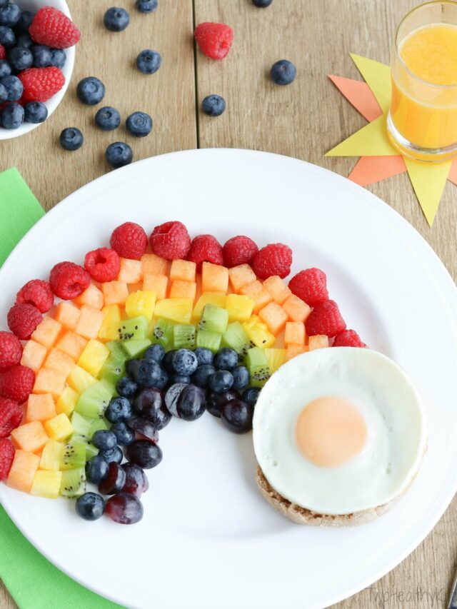 Flatlay of breakfast scene with recipe on white plate, glass of OJ, green napkin and bowl of berries.