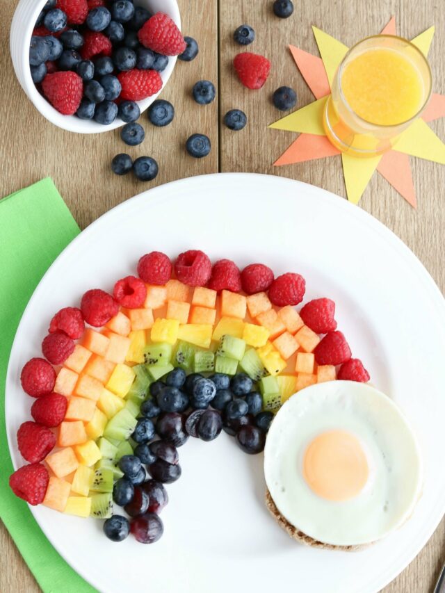 Overhead breakfast scene with plated recipe, green napkin, glass of OJ on sunshine cutout and dish of berries.