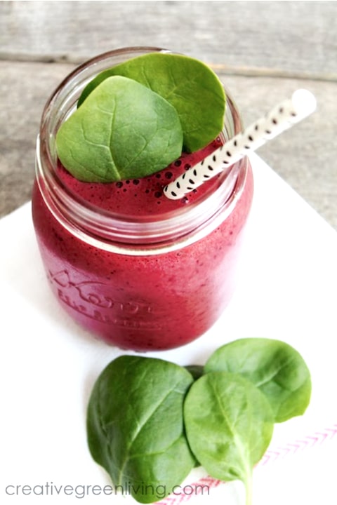 Overhead of dark pink smoothie in jar, garnished with spinach leaves and black-dotted straw.