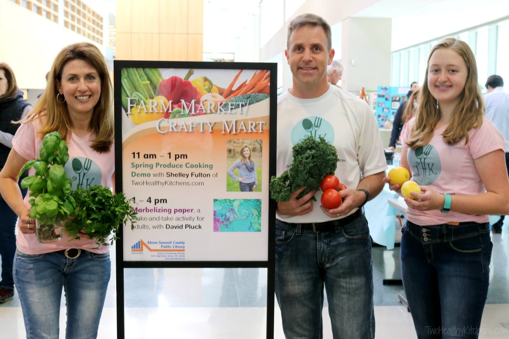 Shelley, Scott and Amy wearing THK logo t-shirts and holding tabouli ingredients next to sign advertising Farm Market.