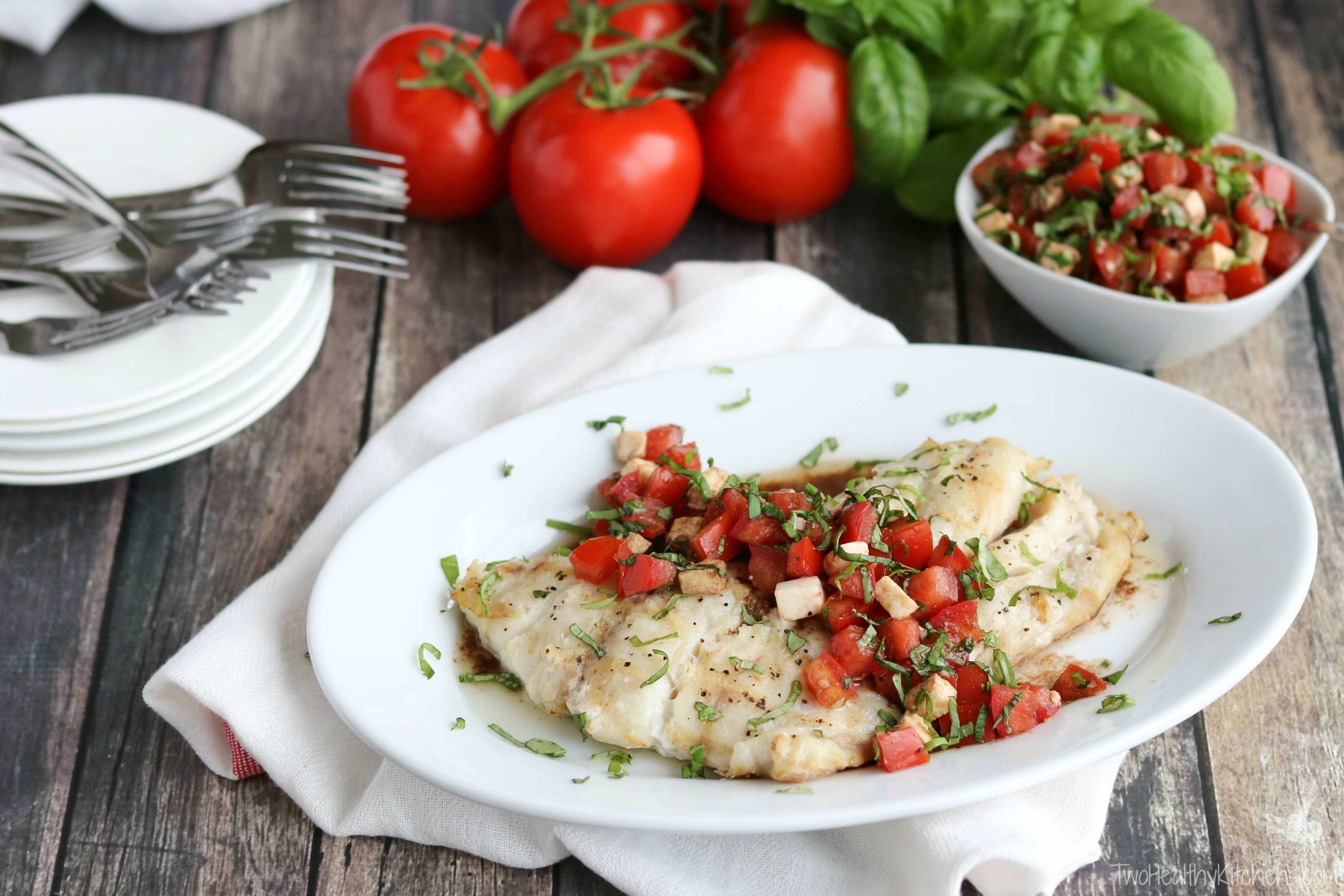 Whole grilled fish filet with caprese topping across, on white serving platter surrounded by ingredients.