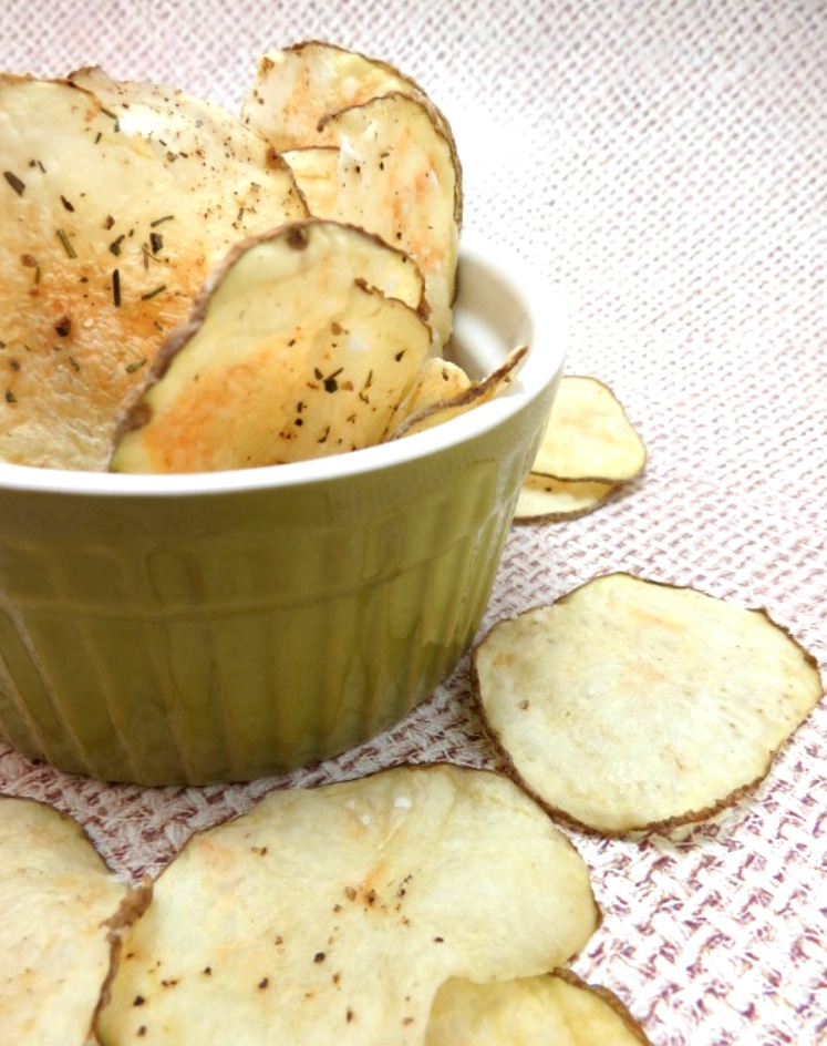 Homemade chips in small, olive-green bowl, with extras scattered nearby.