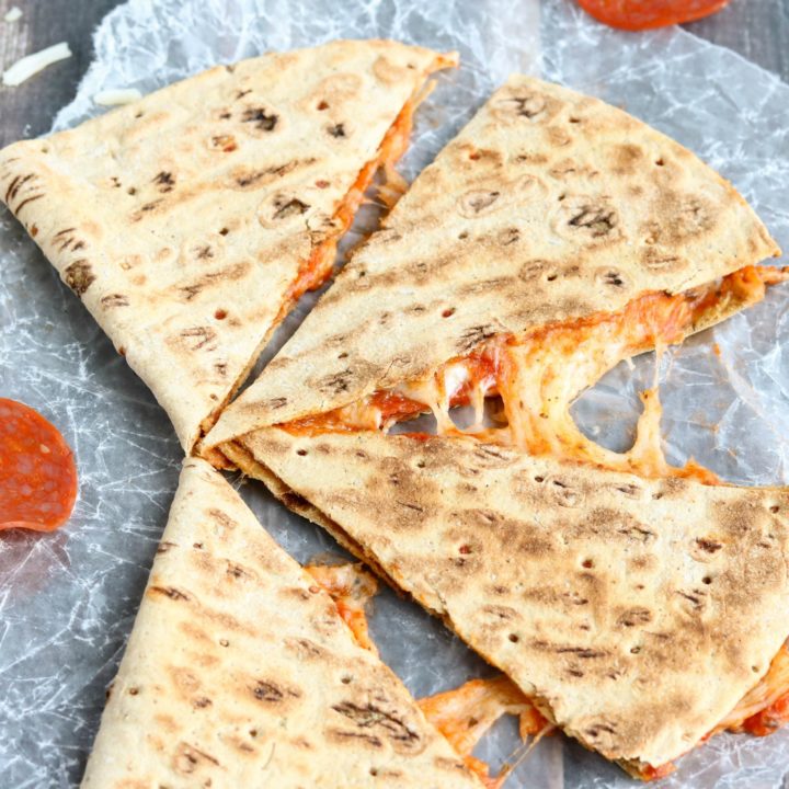 One quesadilla cut into 4 wedges on wax paper, with extra pepperoni and dish of pizza sauce nearby.