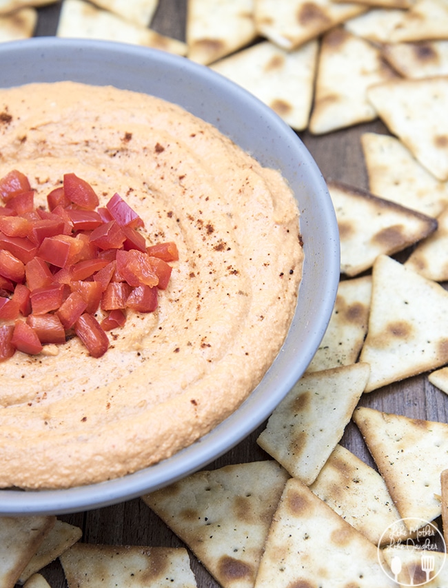 Right side of light blue bowl filled with hummus and surrounded by triangular pita chips.