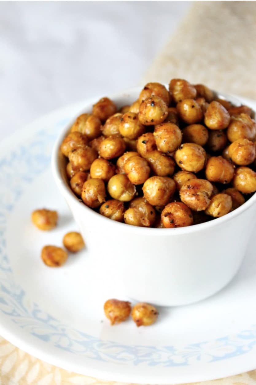 White cup full of roasted chickpeas on plate with blue-patterned rim and tan cloth.