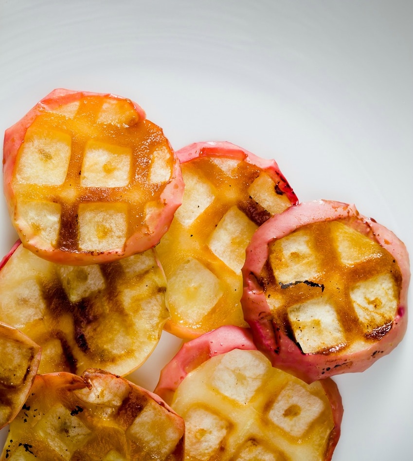 Overhead closeup of several apple slices with waffle iron imprints cooked into them.
