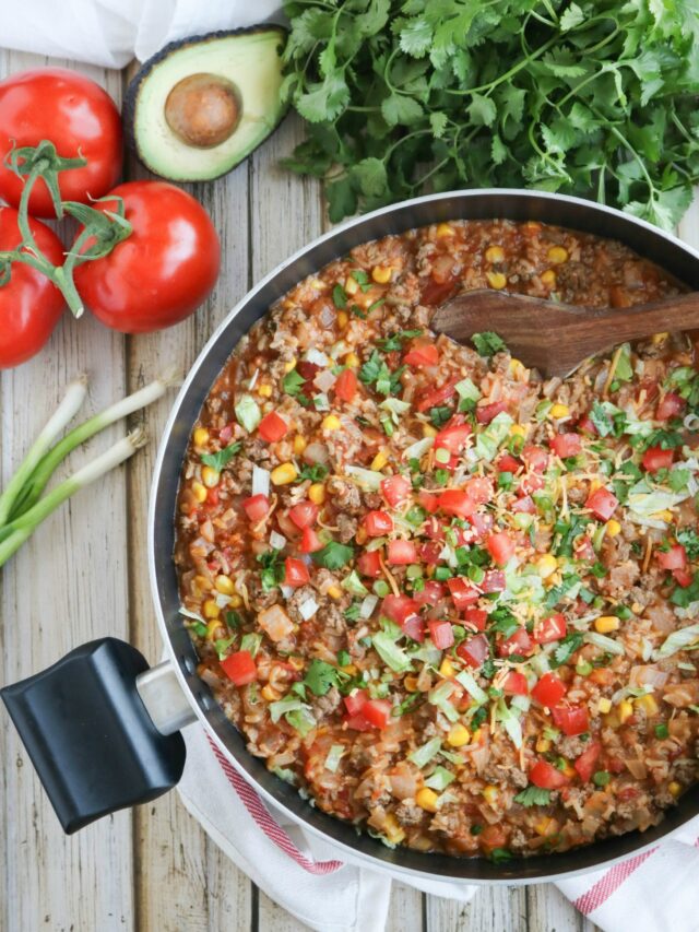 Overhead of recipe in nonstick skillet with wooden spoon dipped at top; additional ingredients nearby.