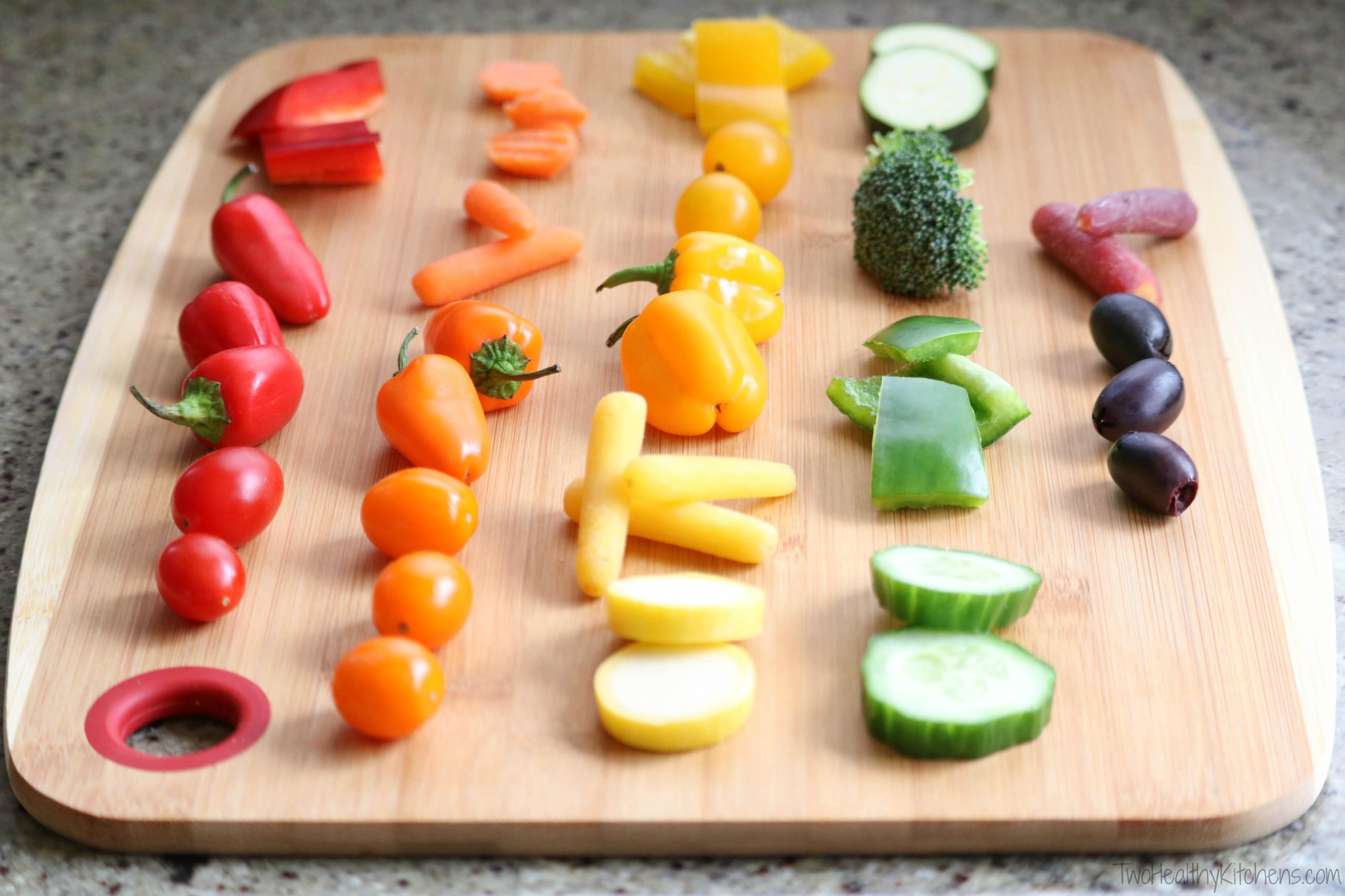 Bamboo cutting board with five lines of color-grouped vegetables: (L to R) red, orange, yellow, green and purple.