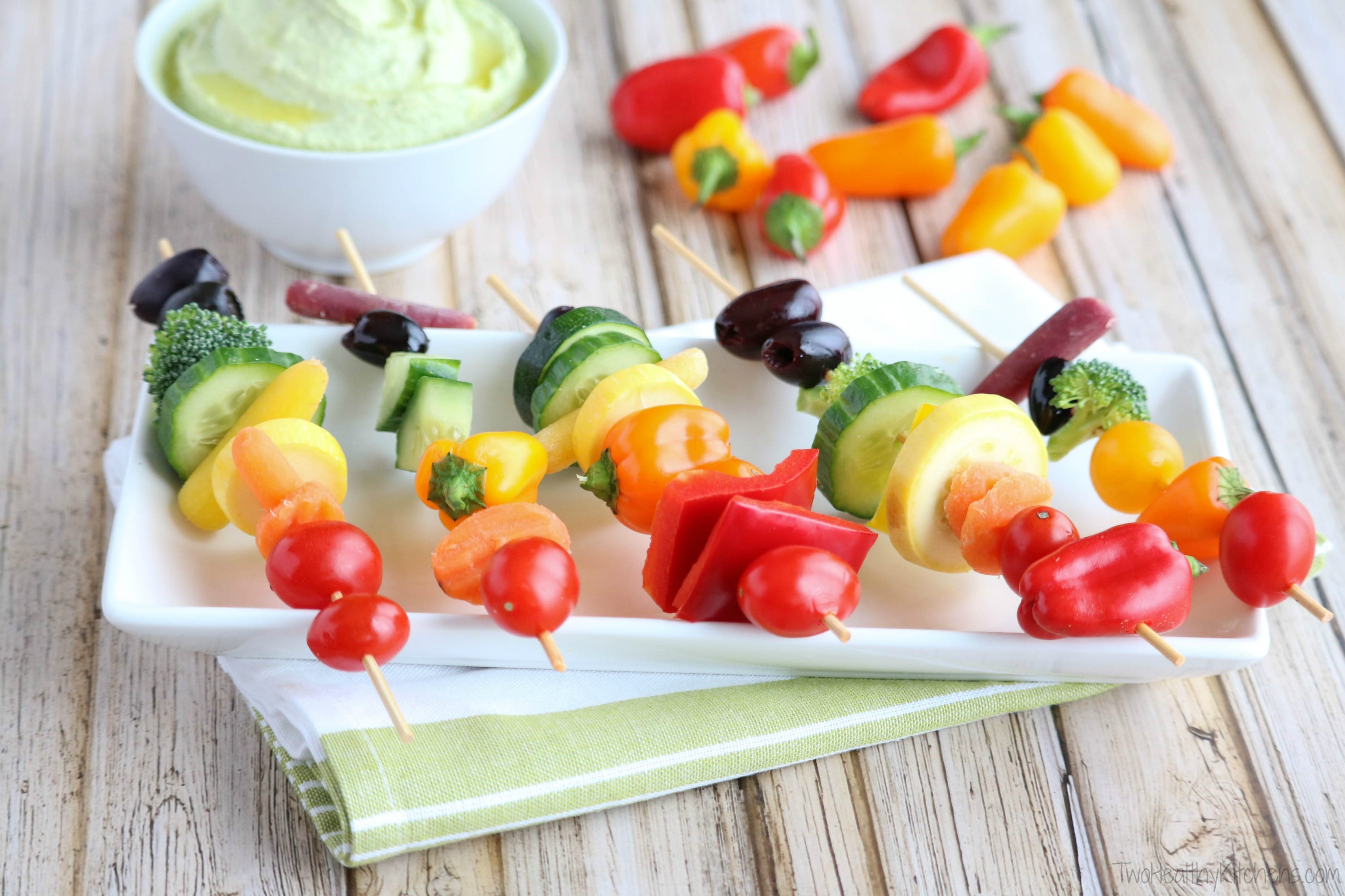 Side view of kabobs with skewers across serving platter, dip and extra vegetables in background.
