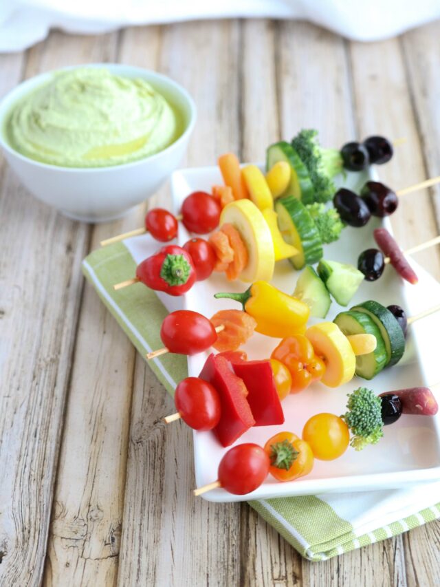 Kabobs presented on white plate on green-stripe cloth with green dip in background.