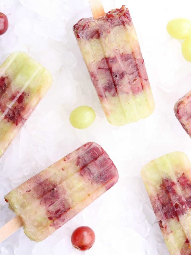 Several frozen pops on bed of ice with whole grapes scattered around.