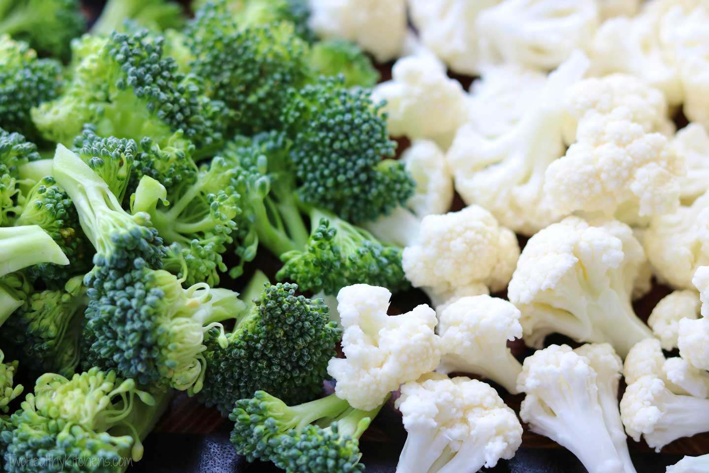 closeup of uncooked veggies - broccoli florets on the left and cauliflower florets on the right