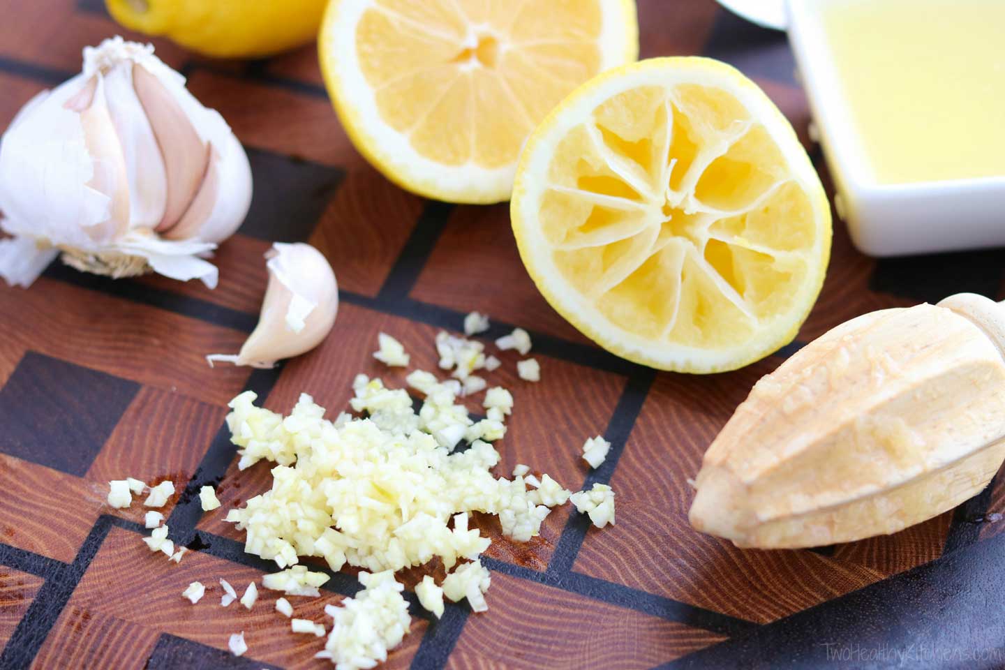 cutting board with garlic cloves and also minced garlic, and with cut lemons with a lemon juicer and a little square bowl of juice