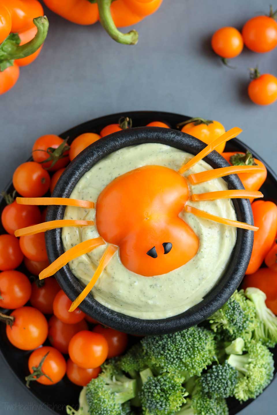 overhead of this ranch dip styled as a Halloween appetizer with a "spider" made out of orange pepper piece perched on top, and green and orange veggies around the dip bowl